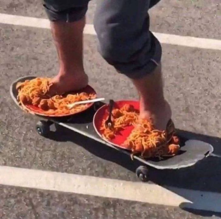 Osoba jazdiaca na skateboarde s nohami v tanieroch špagiet so šatôčkami a vidličkou, kuriózna kompozícia.