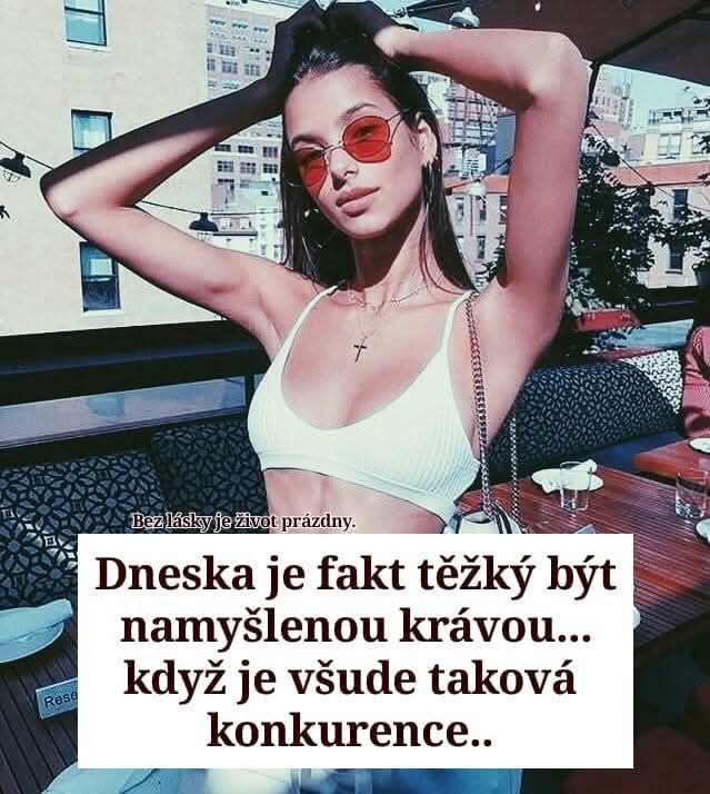 Mladá žena pózuje vonku pri stole, nosí slnečné okuliare a biely top, v pozadí je mesto.