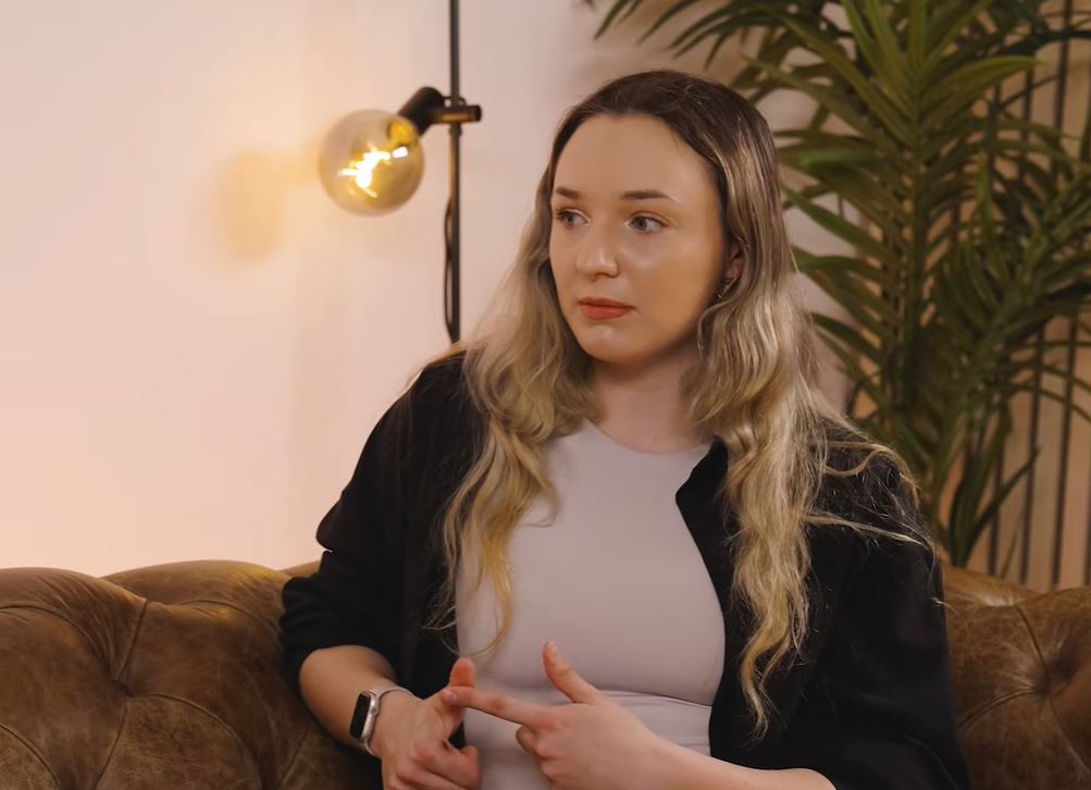 Žena sedí na pohovke v príjemne osvetlenej miestnosti, vedľa rastliny a lampy.