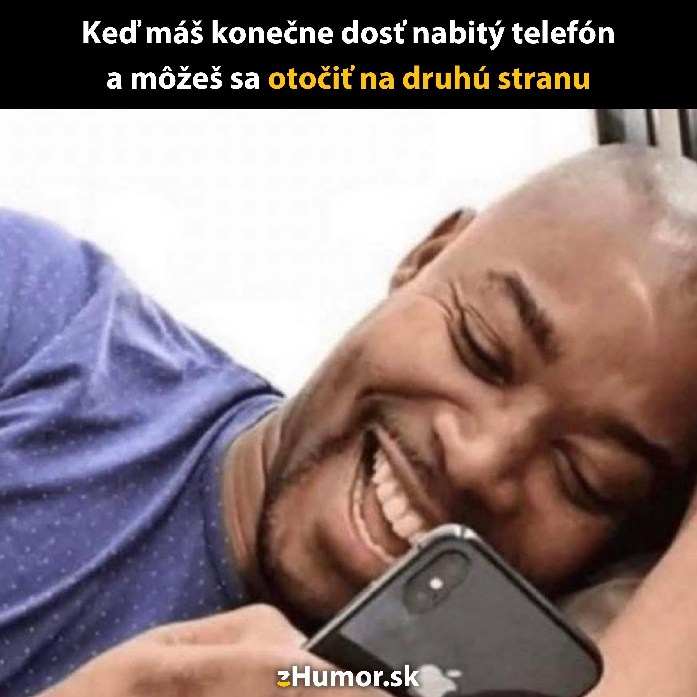 Muž leží na posteli s úsmevom, šťastný z nabitého mobilného telefónu, pripravený otočiť sa na druhú stranu.