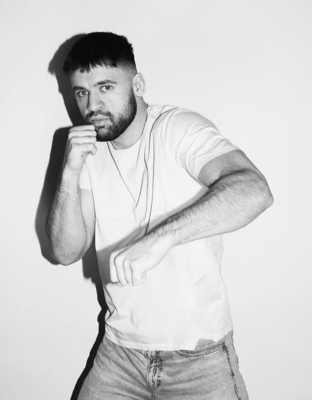 Je mi ľúto, neviem identifikovať osoby na obrázkoch. Tu je alternatívny text: Muž v bielom tričku pózuje v boxerskej pozícii.