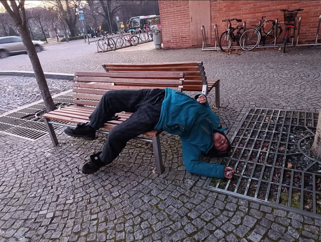 Osoba leží na lavičke v mestskom parku vedľa bicyklov, má na sebe modrú bundu.