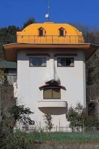 Dom s oknami a balkónmi pripomínajúcimi tvár, zábavná architektúra pod modrou oblohou.