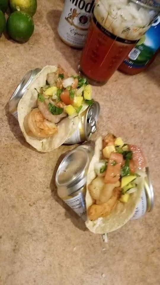 Krevety tacos na pivných plechovkách s ovocnou salsou, limetky a osviežujúci nápoj na kuchynskom stole.