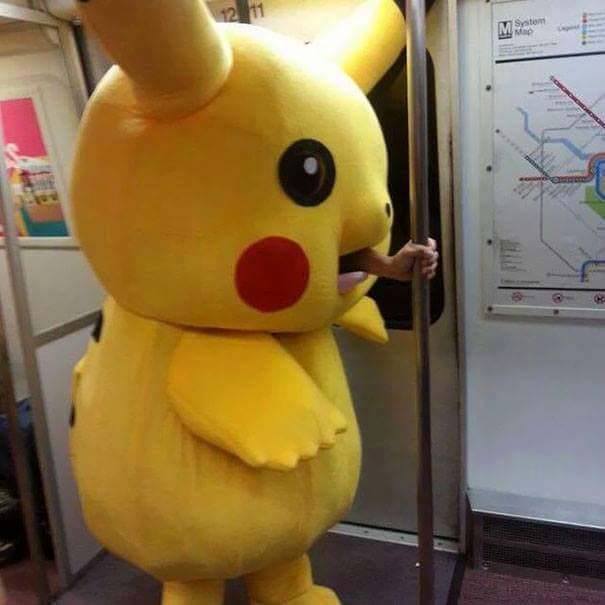Pikachu kostým v metre, človek sa drží tyče a stojí pri schéme trás metra.