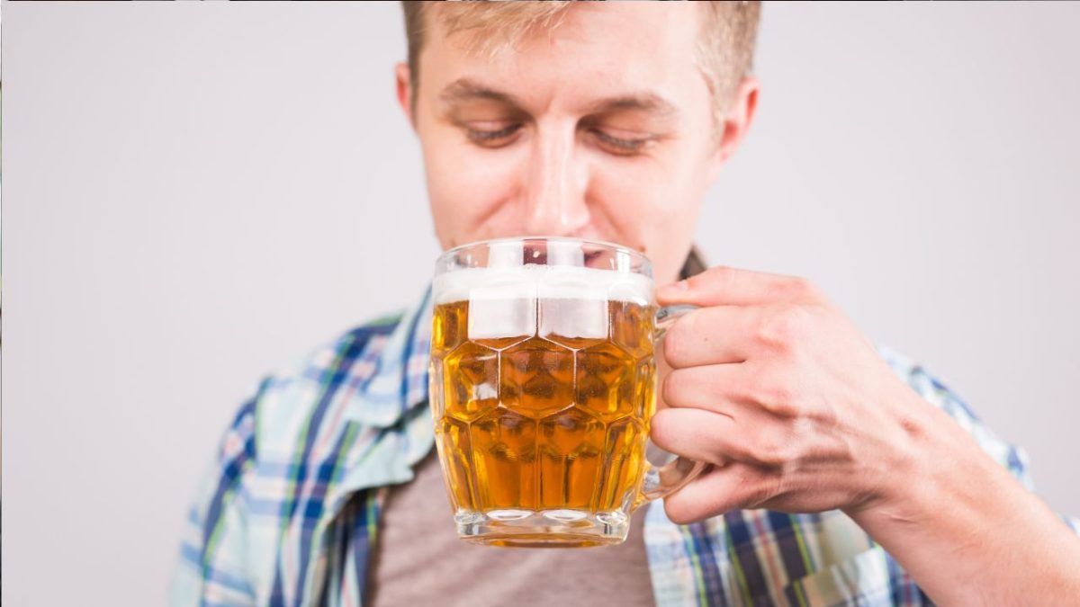 Osoba v károvanej košeli pije osviežujúce pivo z veľkého skleneného pohára.