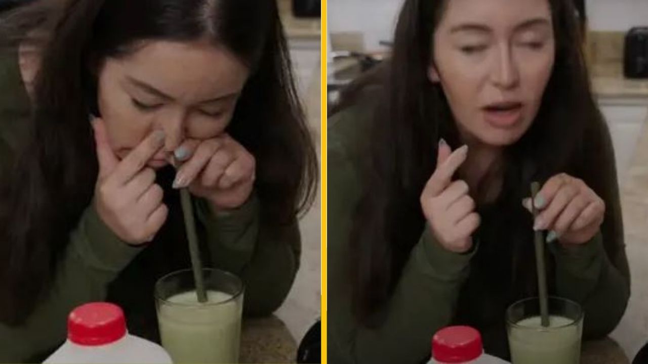 Zvedavá žena skúša piť zelený nápoj cez slamku neobvyklým spôsobom v kuchyni.