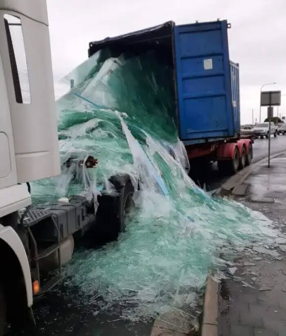 Nehoda nákladného auta s rozbitým sklom na ceste za daždivého počasia, sklo vytečie z kontajnera.