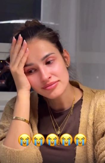 Osoba v svetri s emotívnym výrazom v tvári, rukou si podopiera hlavu, na obrázku sú plačúce emotikony.
