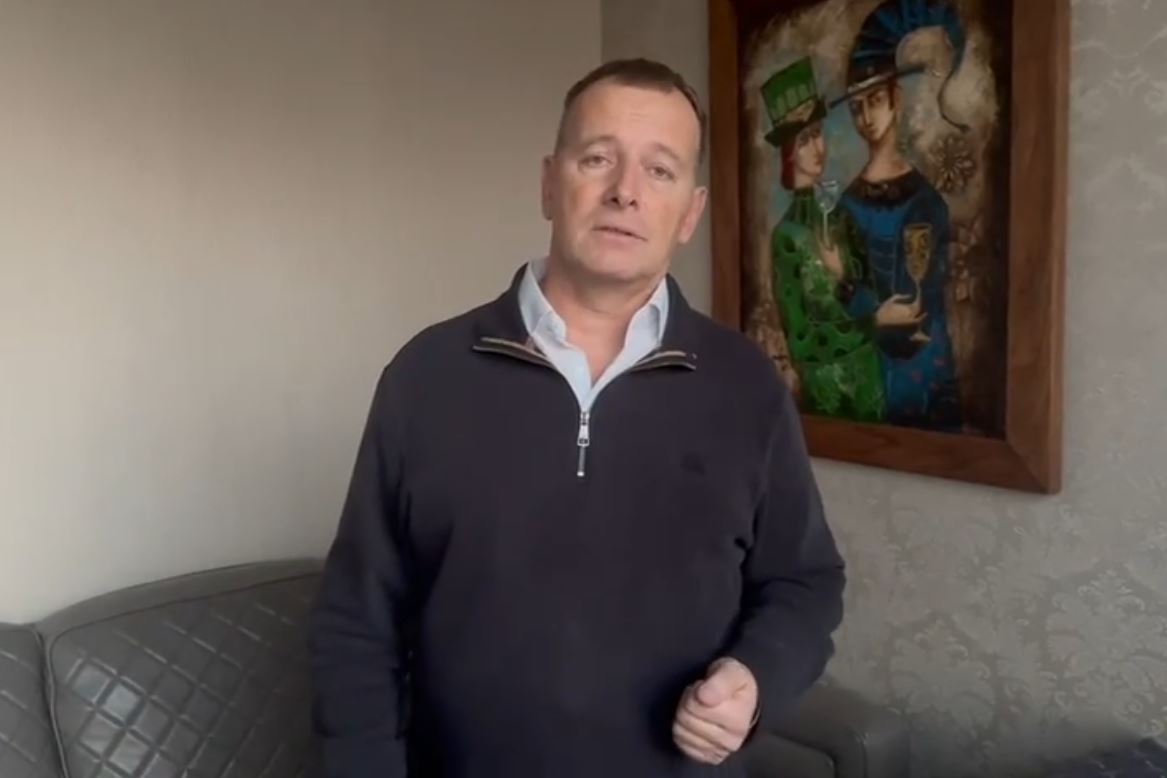 Osoba stojí v obývačke vedľa pohovky s obrazom na stene, oblečená v tmavom svetri.