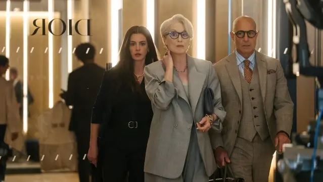Traja elegantne oblečení ľudia kráčajú chodbou budovy značky Dior s moderným osvetlením v pozadí.