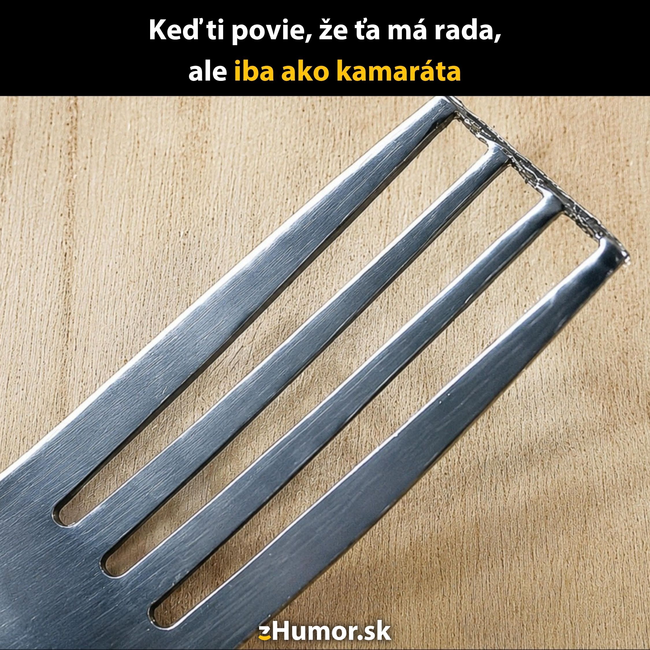 Vidlička s tromi plnými a jedným prázdnym zubom na drevenom povrchu, s humorným textom o priateľskej zóne.