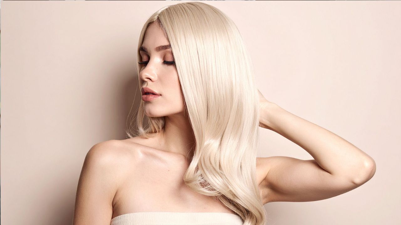 Blond žena s dlhými vlasmi v elegantnej póze na svetlom pozadí.