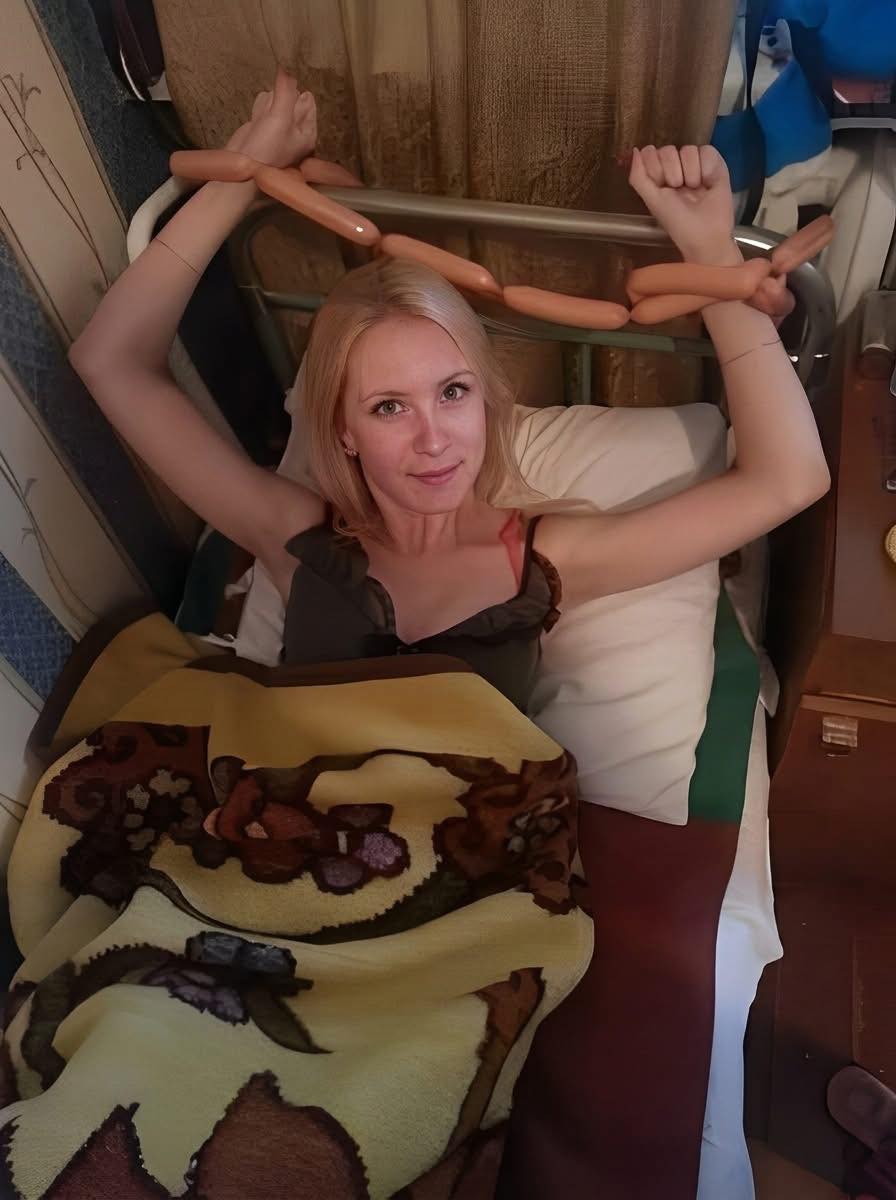 Žena s úsmevom v posteli s dekou v netradičnej situácii s párkami na rukách.