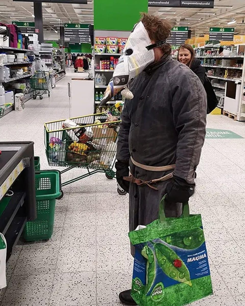 Muž v obchode nosí kreatívnu ochrannú masku, tlačiaci plný vozík s potravinami, bojujúci proti pandémii.