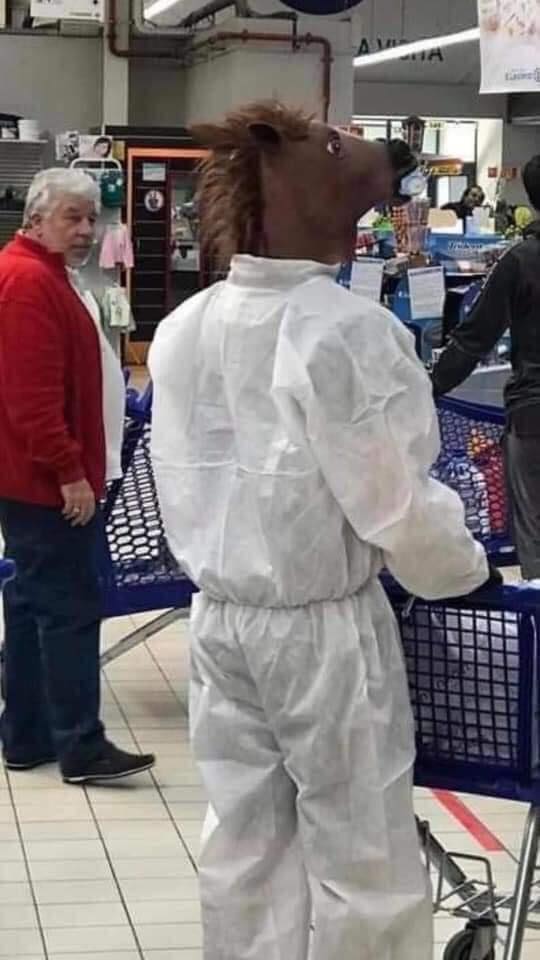 Osoba v bielom overale a maske koňa s nákupným vozíkom v supermarkete, zaujatá pozornosť zákazníka.