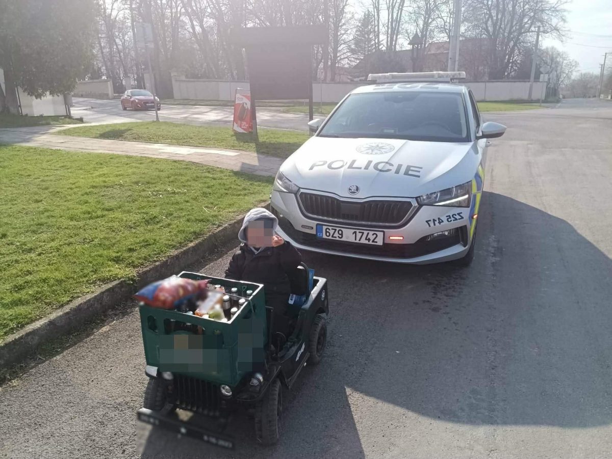 Dieťa v elektrickom autíčku pred policajným vozidlom na ulici.