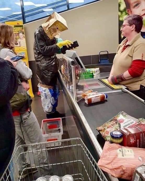 Zákazník s provizórnym oblečením platí pri pokladni v supermarkete, vzbudzujúc pozornosť ostatných.