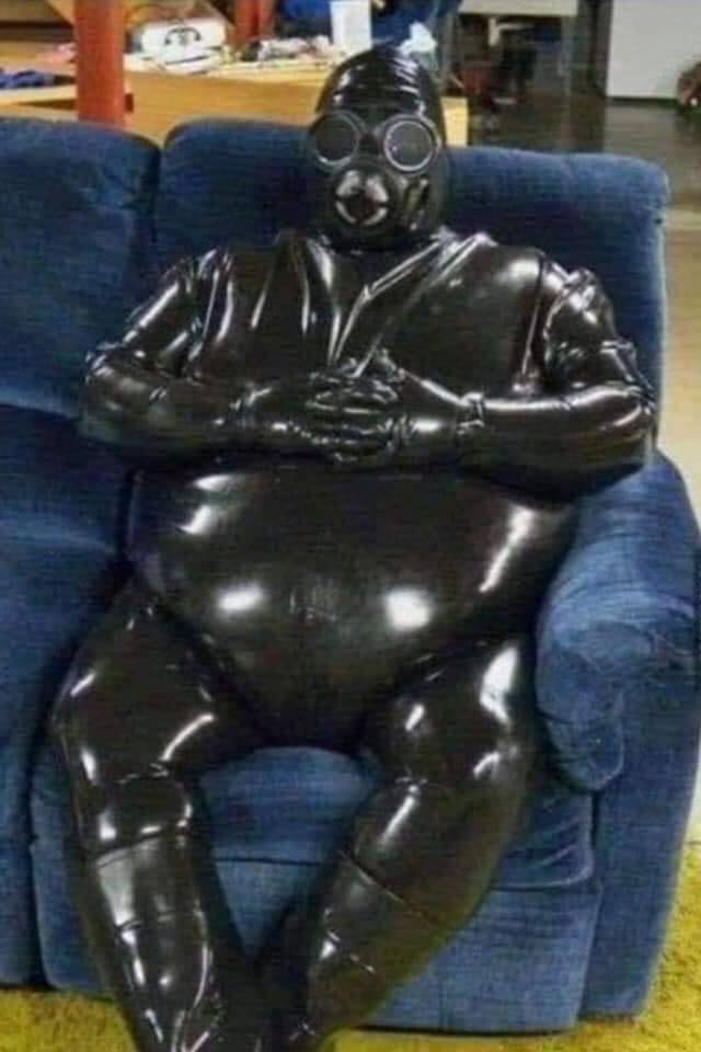 Ľudia v latexovom obleku sedia na modrej pohovke, interiér miestnosti na pozadí.
