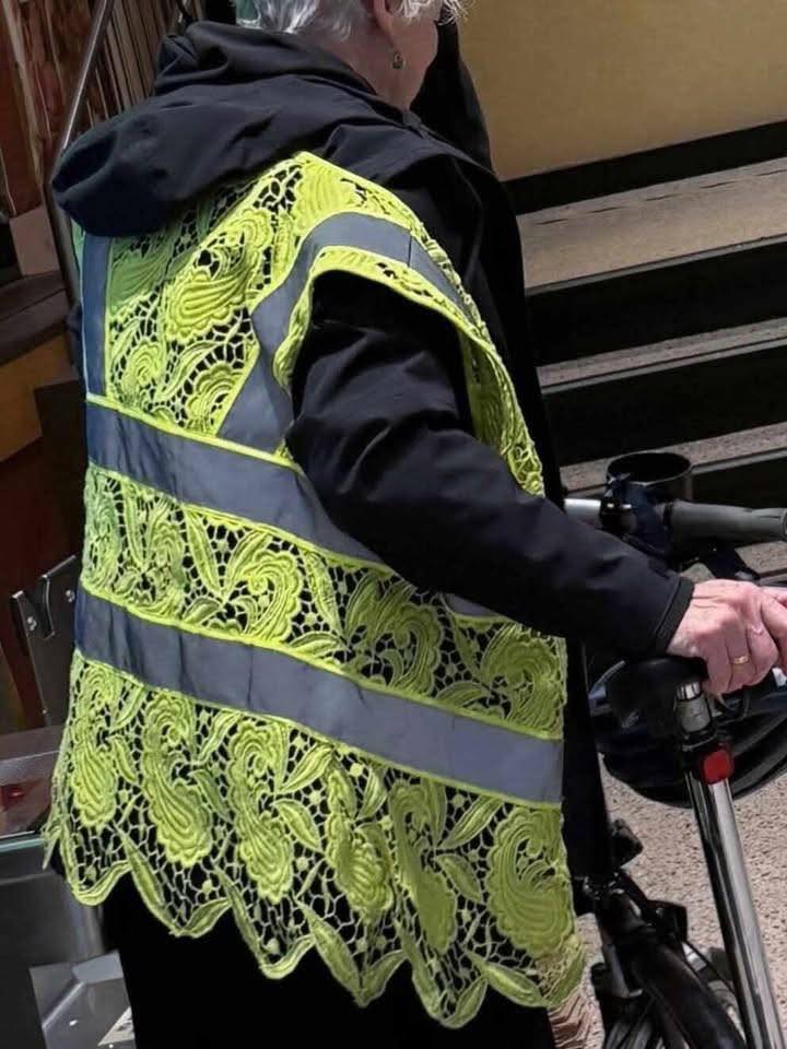 Staršia dáma so svietivou zelenou vestičkou s čipkovaným vzorom pri bicykli vo vnútornom priestore.