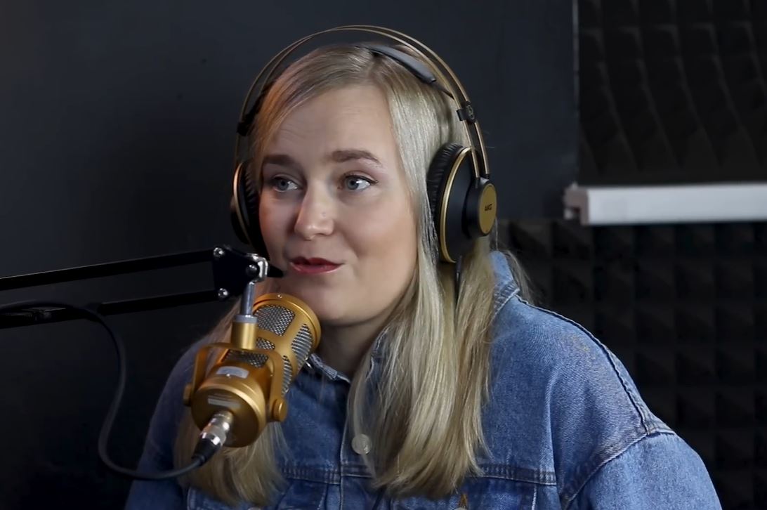 Žena s blond vlasmi a slúchadlami nahráva podcast v štúdiu s mikrofónom.