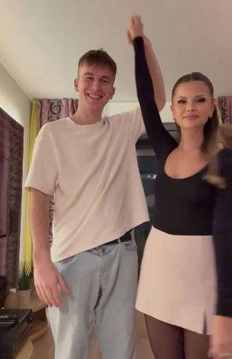 Mladý pár tancuje v obývačke, muž v bielom tričku, žena v čiernom tope a béžovej sukni, usmievajú sa.