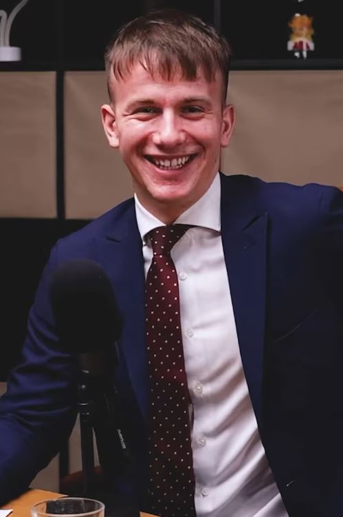 Osoba v obleku s mikrofónom sedí v štúdiu počas nahrávania podcastu.