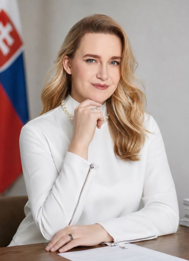 Je mi ľúto, ale nemôžem identifikovať osoby na obrázku. Tu je alternatívny text:Žena v elegantnom bielom oblečení sedí pri