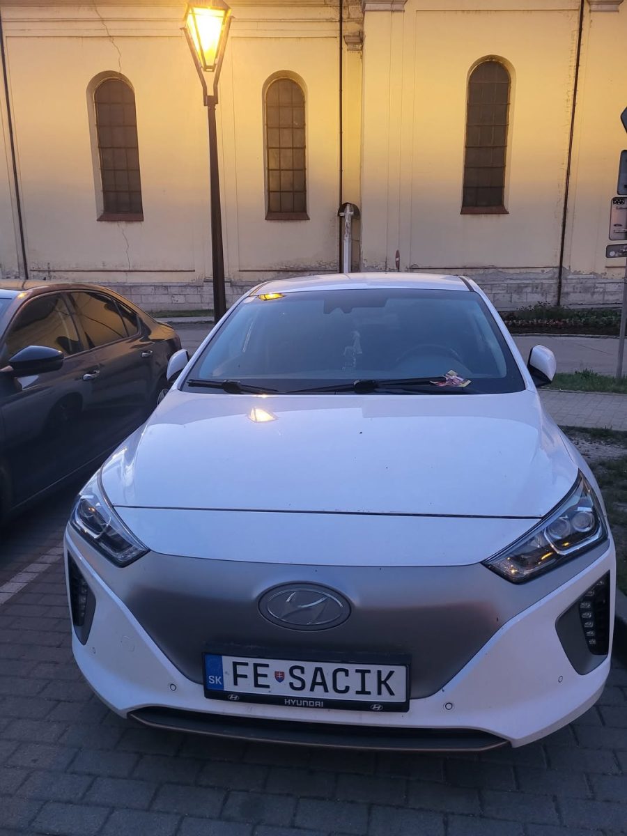 Biely Hyundai zaparkovaný na ulici pri historickej budove za súmraku, osvetlený pouličnou lampou.