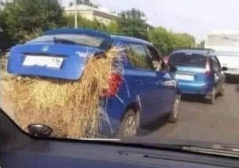Modré auto so slameným nákladom vyčnievajúcim z kufra stojace v premávke na ceste.