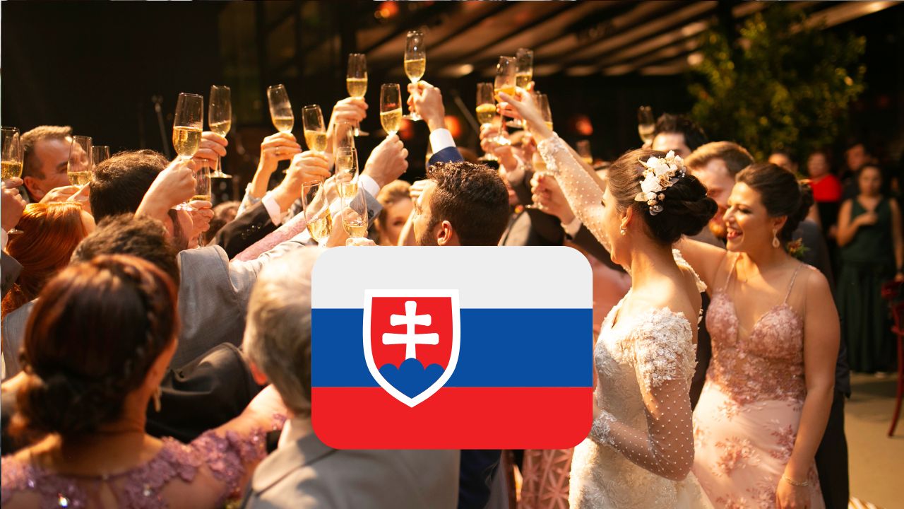 Slovenská svadba: Skupina svadobčanov dvíha poháre na prípitok, vlajka Slovenska na popredí.