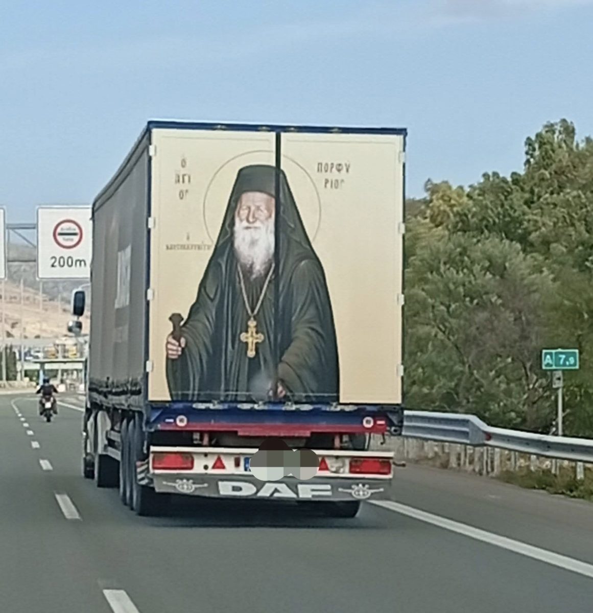 Náklaďák na diaľnici s obrazom ortodoxného duchovného na zadnej časti, vedľa cesty dopravné značky.