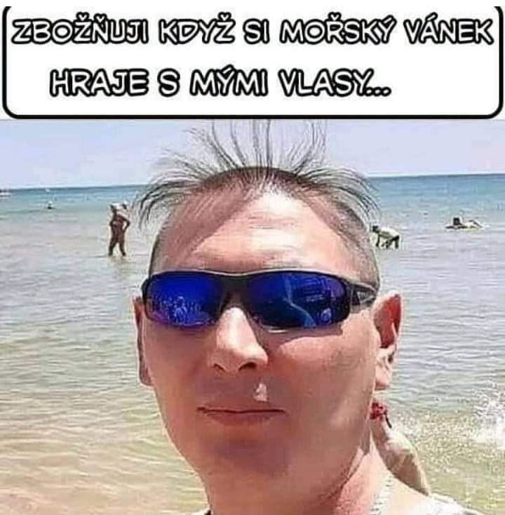 Osoba na pláži s vetrom vo vlasoch a s nápisom Zbožňuji když si mořský vánek hraje s mými vlasy.