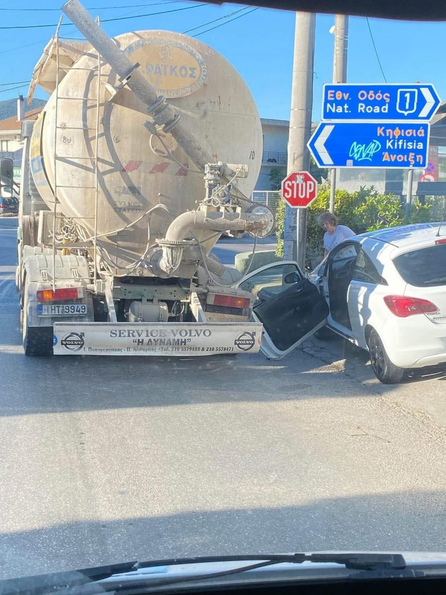 Nákladné auto a biele auto na križovatke pri značke STOP počas dňa. Dopravná situácia a navigačná tabuľa.