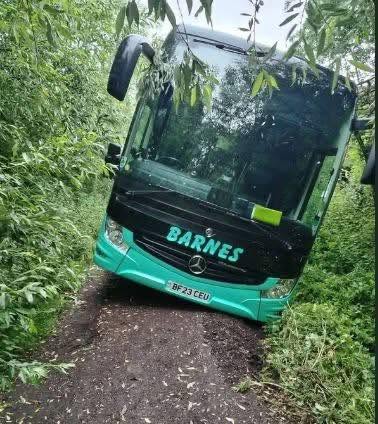 Autobus uviaznutý na úzkej lesnej ceste obklopený zeleňou.