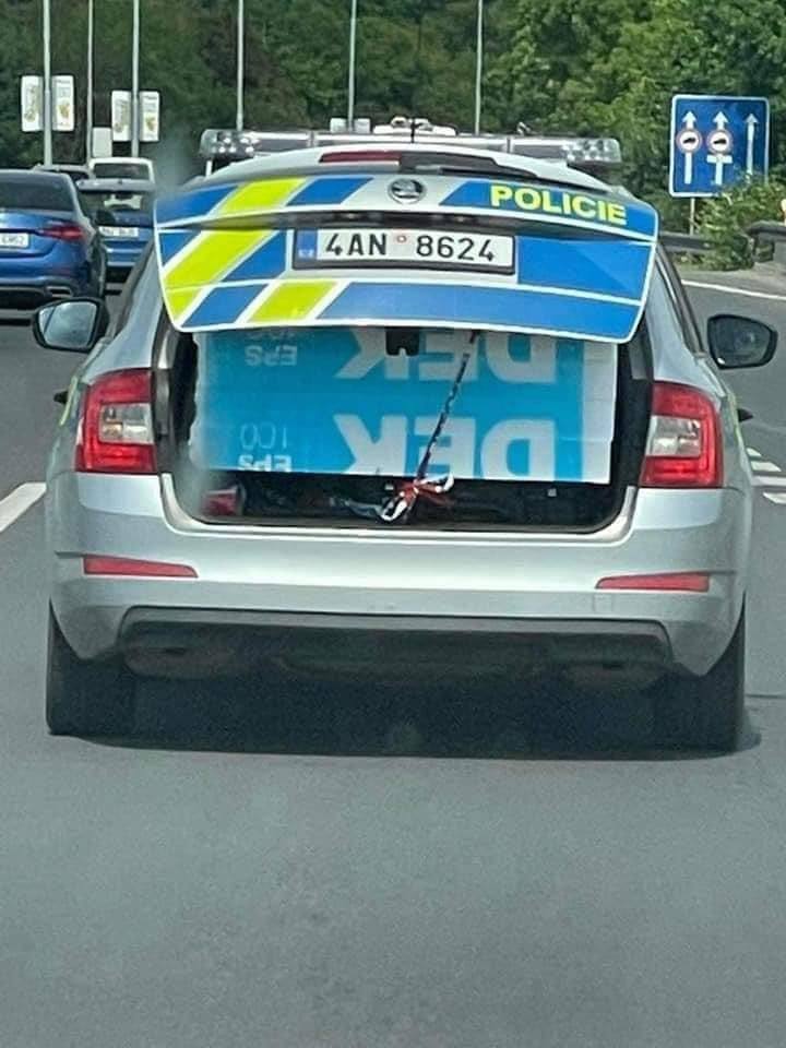 Policejné auto s otvoreným kufrom na ceste, preváža objemný náklad prekrytý plachtou.