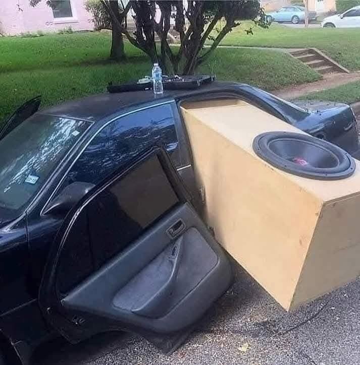 Auto s veľkým subwooferom presahujúcim cez otvorené zadné dvere na ulici.
