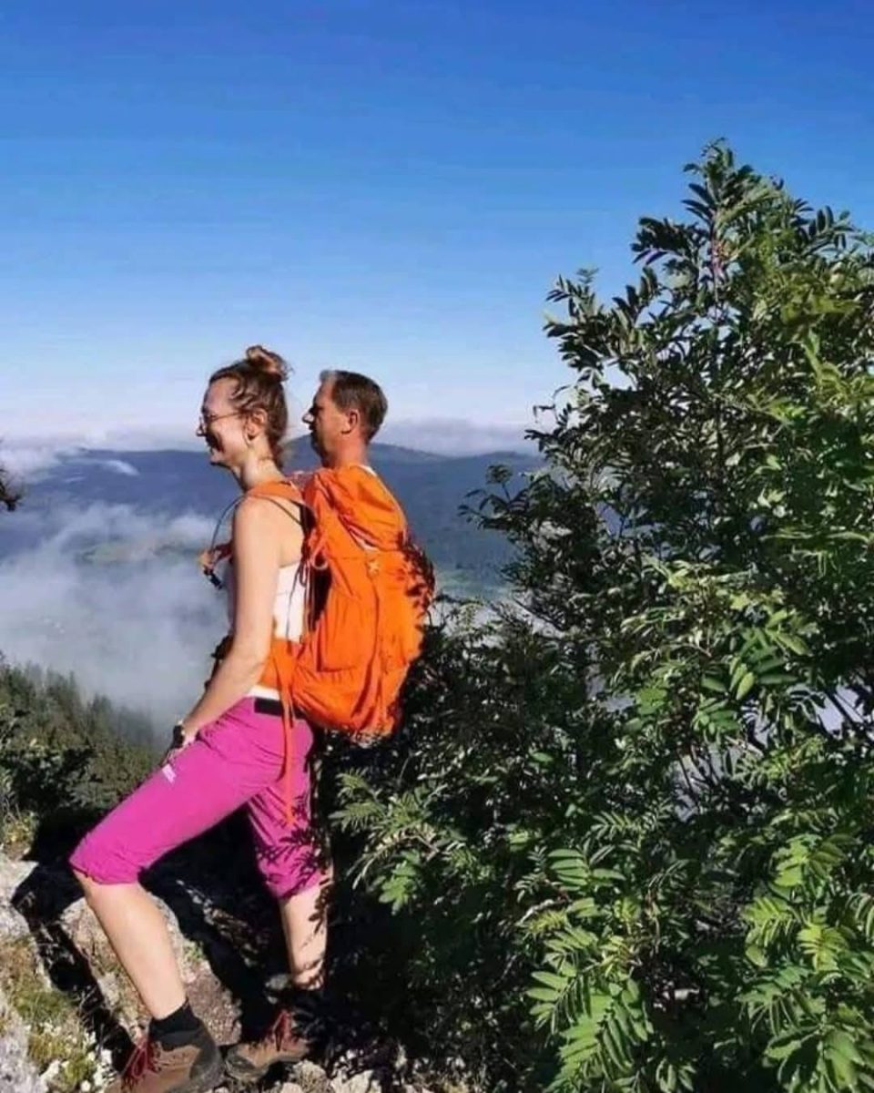 Turisti s batohmi na horskej túre v slnečnom počasí, s výhľadom na hory a oblaky.