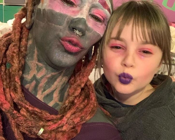 Dve osoby s extravagantným make-upom a farebnými vlasmi pózujú s úsmevom a pestrofarebným líčením.