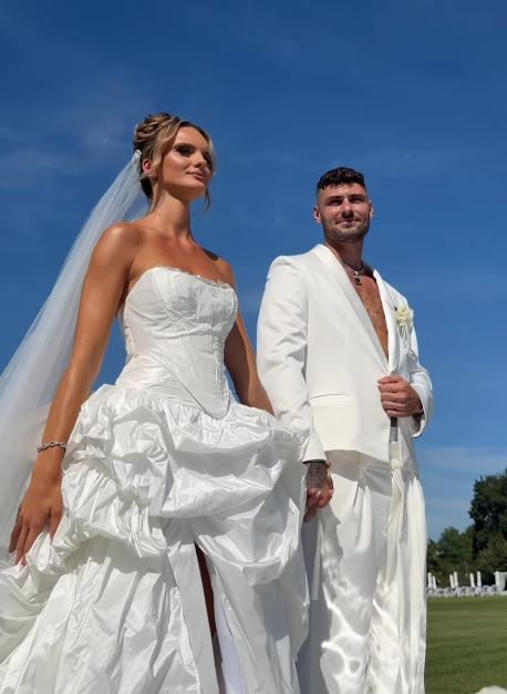 Nevesta a ženích v bielom na letnej svadbe, stojaci vonku na zelenej lúke pod modrou oblohou.