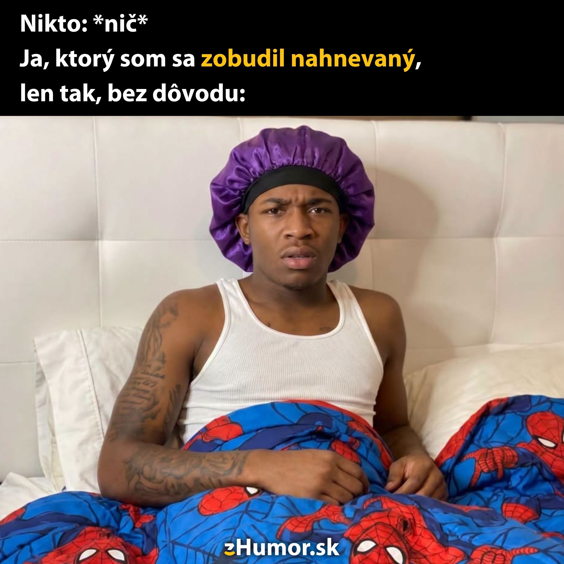 Muž v posteli, oblečený v tielku a čiapke, s prekvapeným výrazom, obklopený Spiderman perinou.