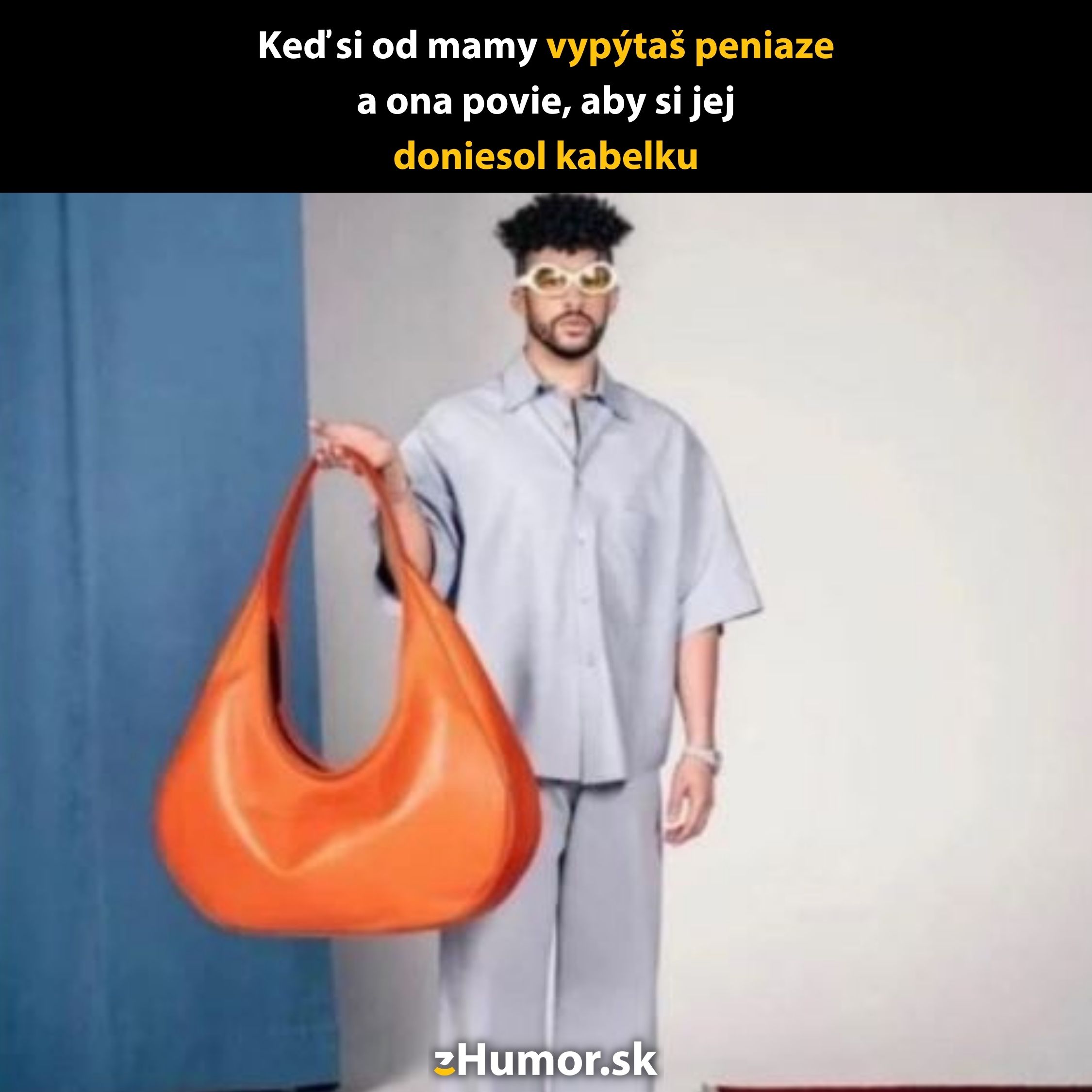 Muž v šedom oblečení drží veľkú oranžovú kabelku, so zábavným textom o peniazoch od mamy.