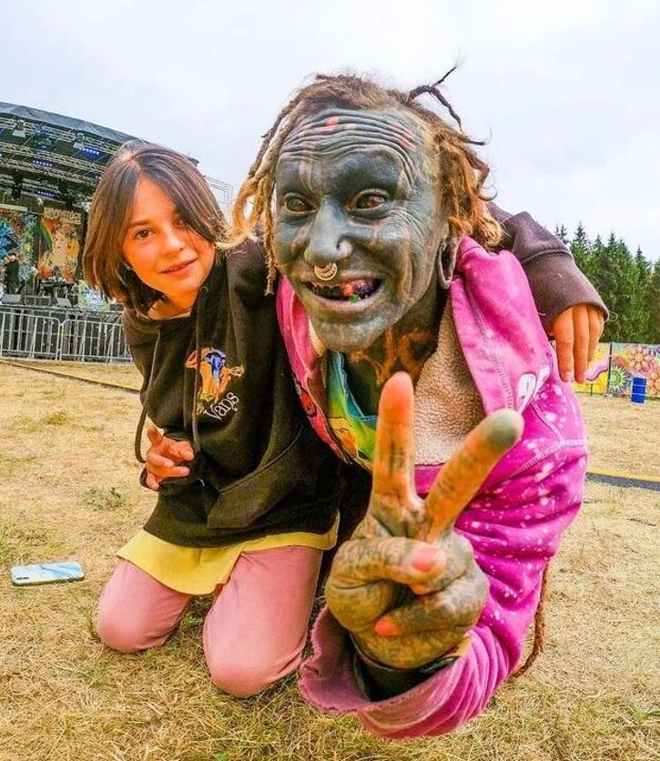 Dve osoby na festivale s hudobným pódiom v pozadí, pokojový znak.