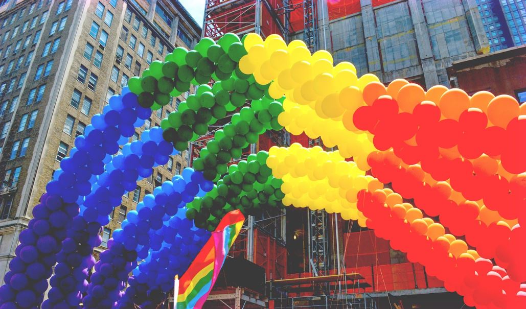 Pestrofarebné balónové oblúky nad mestskou ulicou počas Pride festivalu.