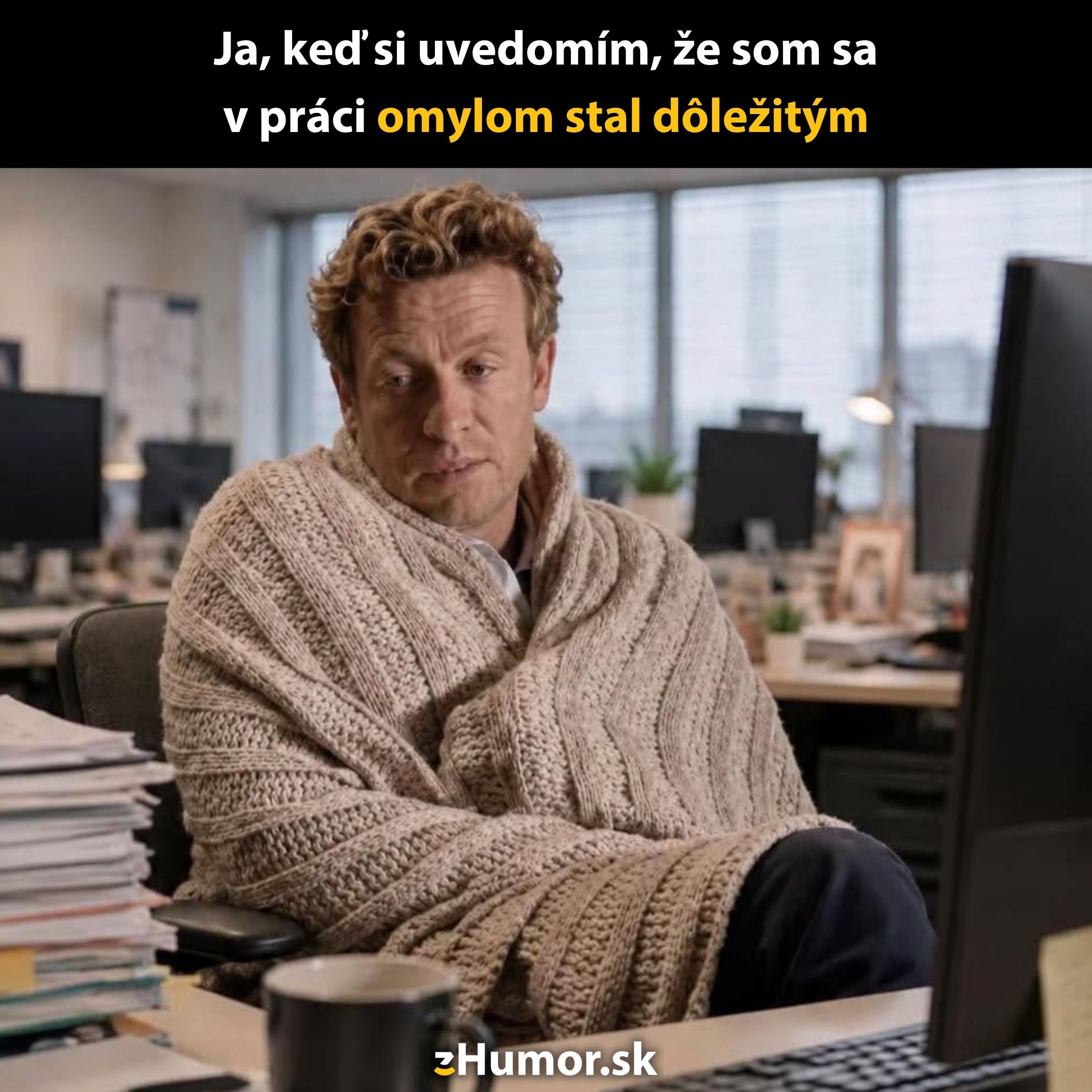 Muž v kancelárii pod dekou, obklopený papiermi, vyjadruje prekvapenie nad svojou dôležitou úlohou v práci.