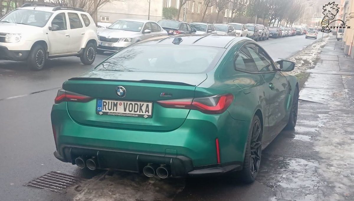 Zelené BMW s poznávacou značkou RUM VODKA zaparkované na ulici vedľa ďalších áut, zima, mierne zasnežené chodníky.