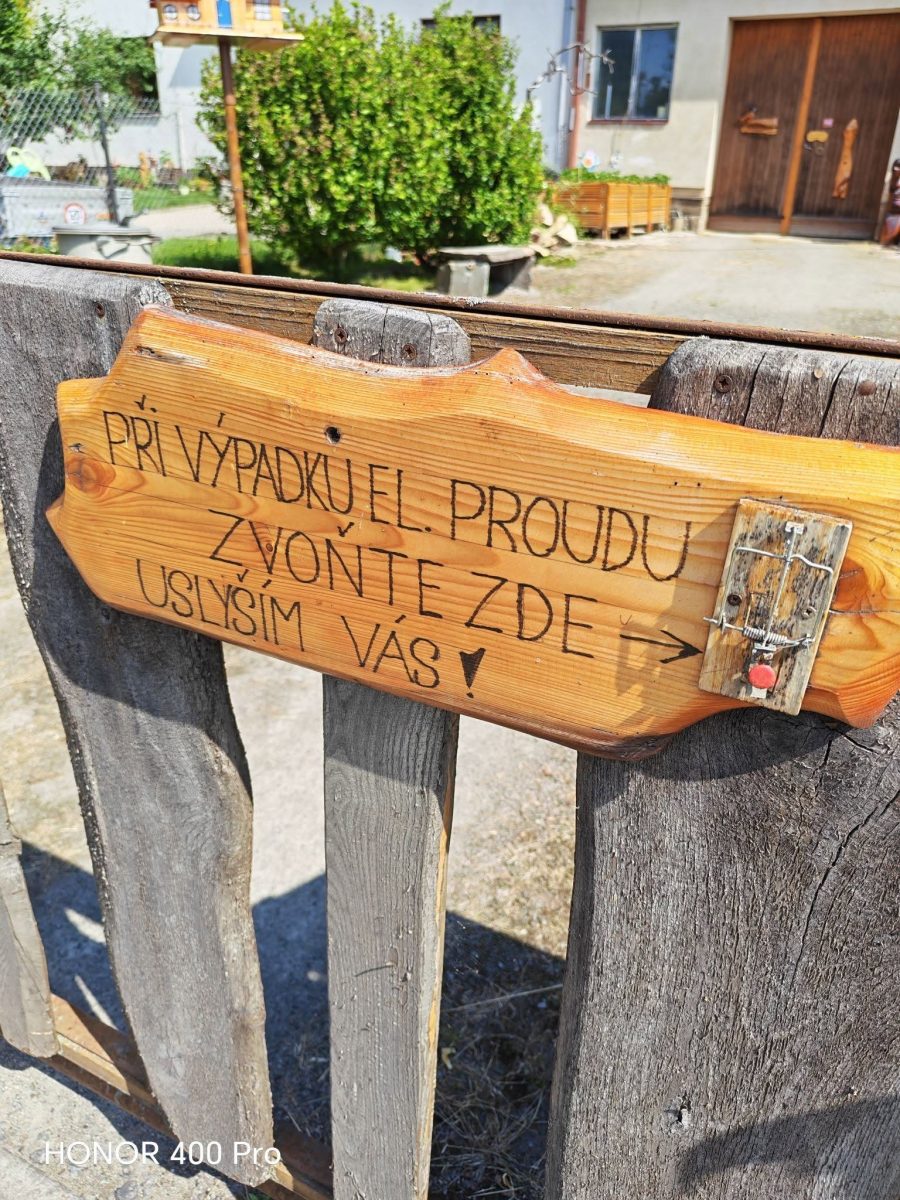 Drevená tabuľa na plote s inštrukciou na zvonenie v prípade výpadku elektrického prúdu.