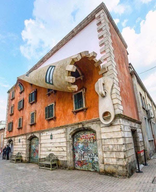 Budova s ilúziou obrovského zipsu na stene, kreatívna architektúra s oranžovou omietkou a zvláštne dizajnové prvky.