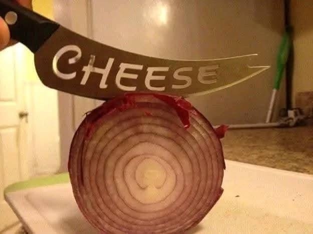 Nôž s nápisom cheese krája červenú cibuľu na kuchynskej doske.