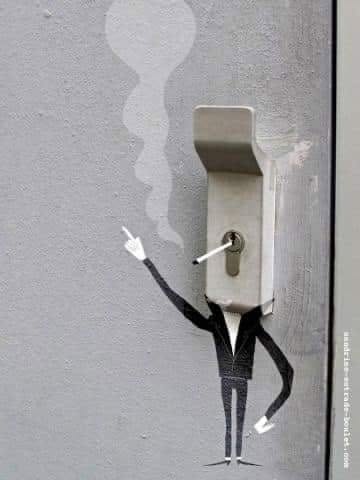 Kreatívne street art dielo: kreslená postava fajčiacej cigarety s klobúkom v podobe kľúčovej dierky na šedom podklade.